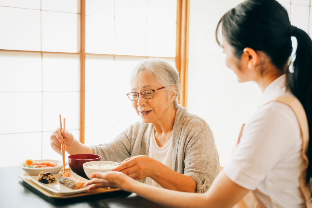 食事をする高齢者女性と女性スタッフ（笑顔）