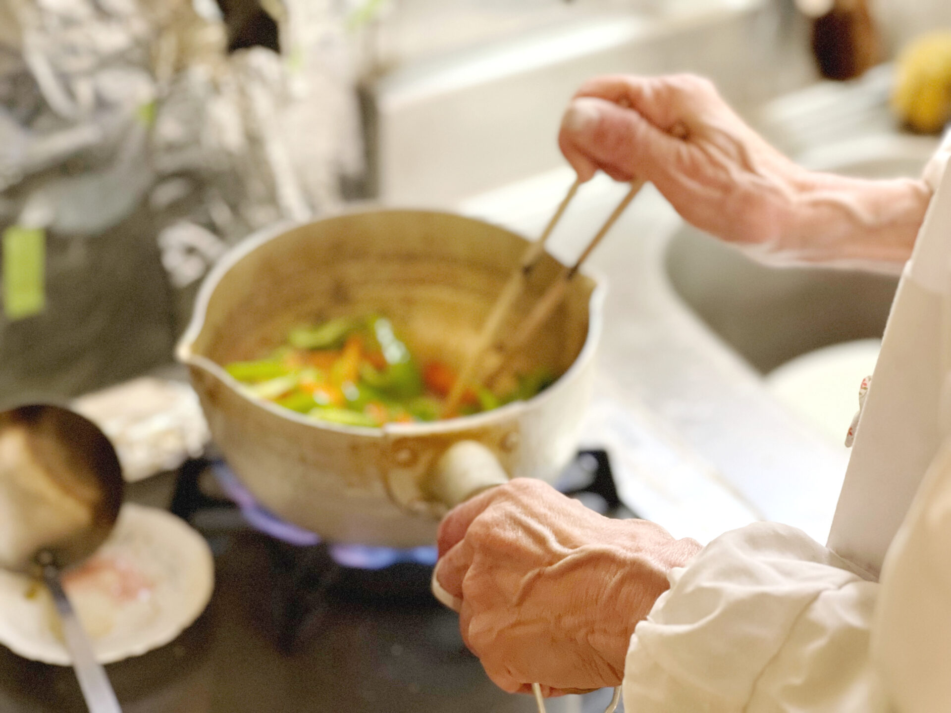 台所で炒め物をする高齢女性の手
